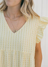 Close up of model wearing a yellow tone on tone checked dress with capped short sleeves.