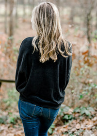Back view of Blonde model wearing black V-neck sweater.