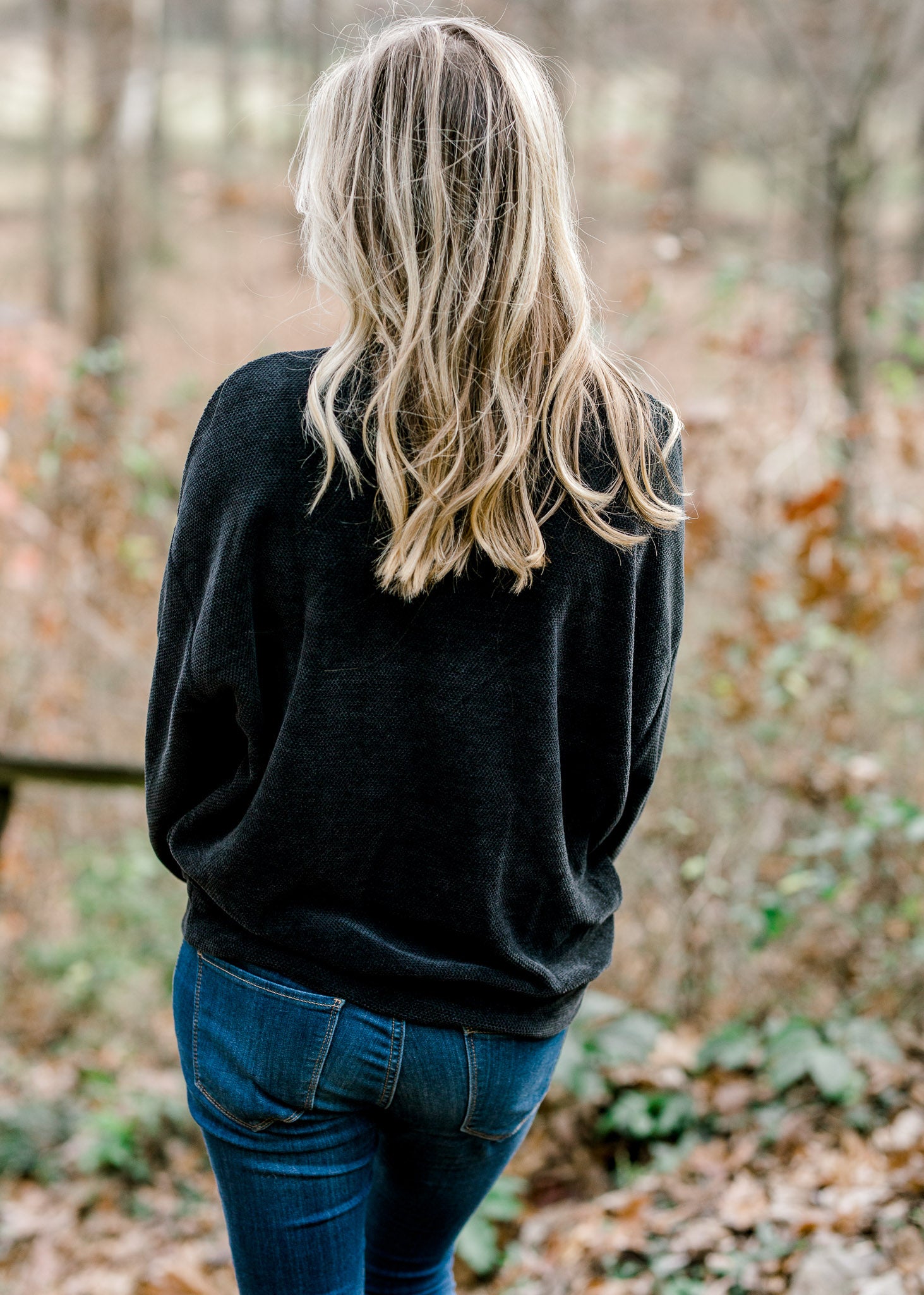 Back view of Blonde model wearing black V-neck sweater.