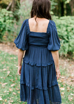 back view of Brunette model wearing a navy midi dress with smocked bodice.