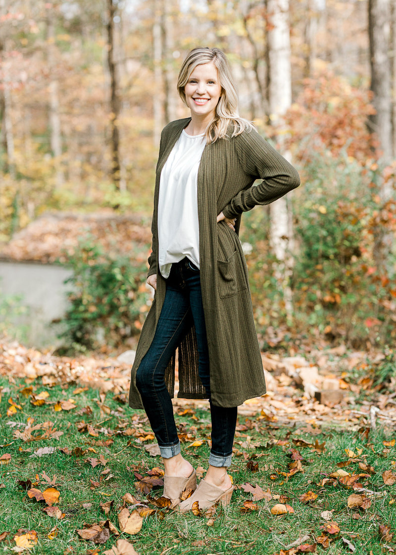 Blonde model wearing a dark green cardigan with a white top, jeans and heeled mules. 