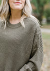 Close up view of Blonde model wearing olive cable knit sweater.