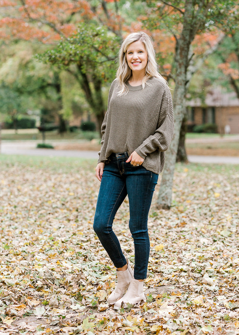 Blonde model wearing olive cable knit sweater with jeans and booties.