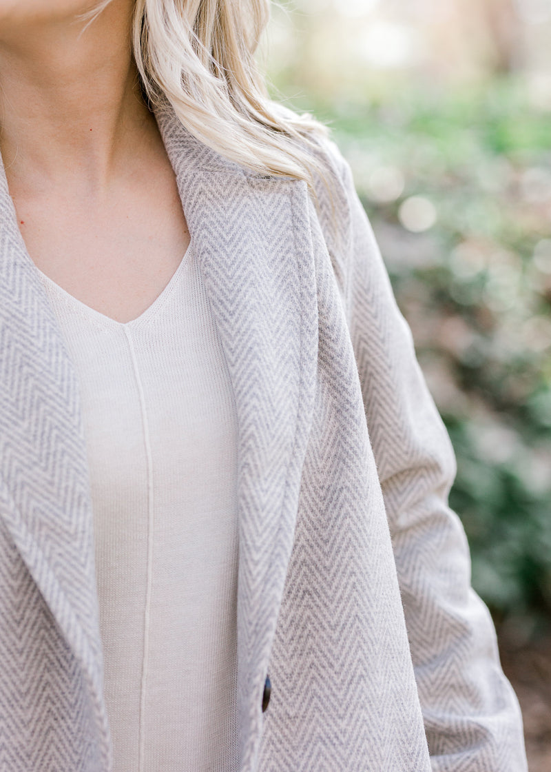 Close up view of blonde model is wearing herringbone coat. 