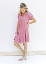 Model wearing an above the knee rose colored dress with bubble short sleeves and a tie at the neck. 