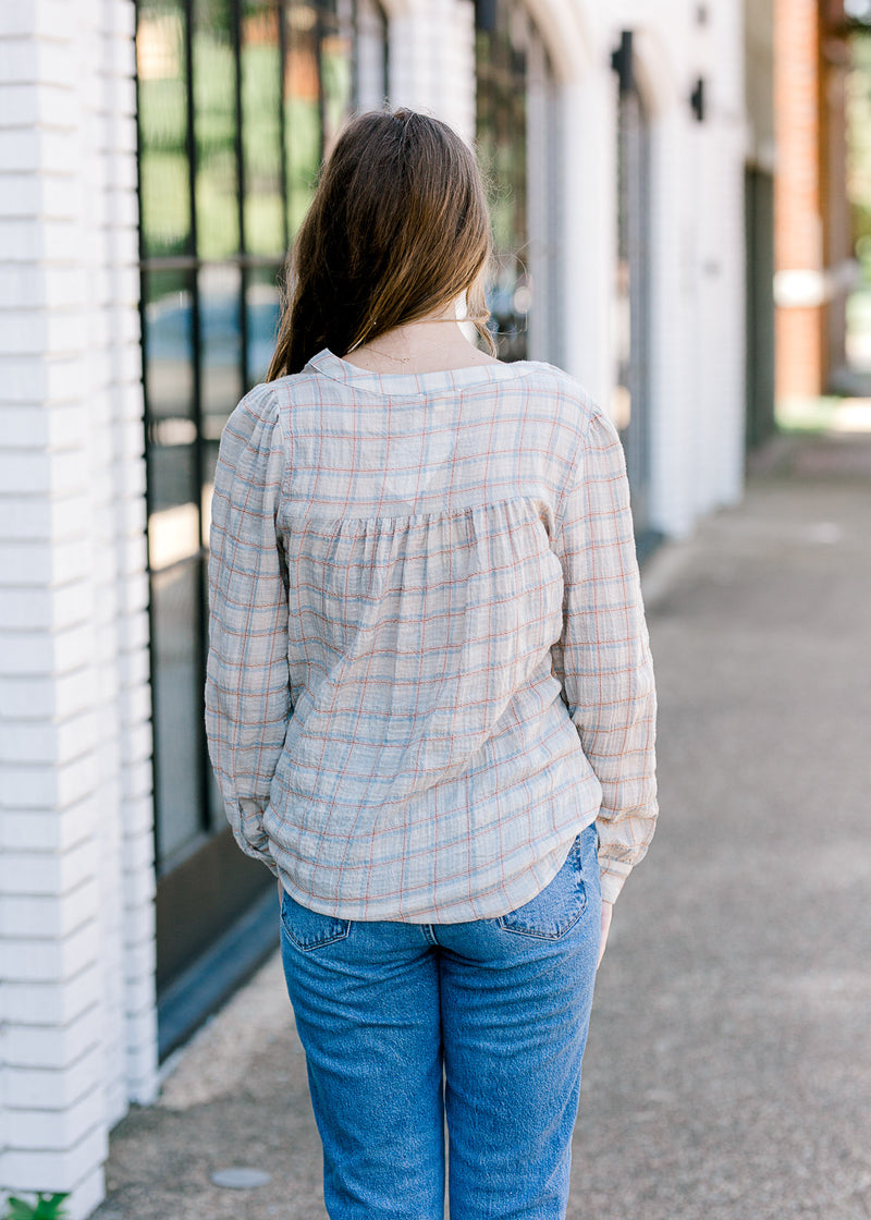 Back view of Brunette model wearing taupe, rust, and blue plaid top.