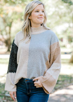 Blonde model wearing light gray, dark gray, taupe and camel color block sweater. 