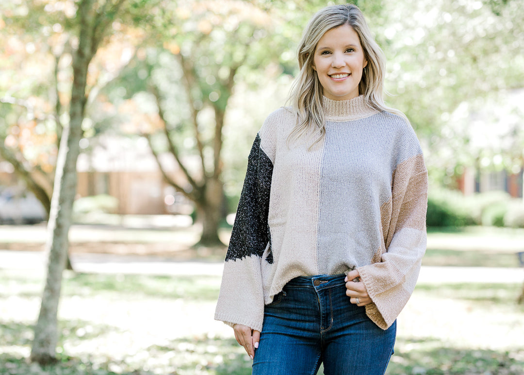 Blonde model wearing light gray, dark gray, taupe and camel color block sweater with jeans.
