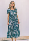 Model wearing a turquoise midi dress with a cream fern pattern. 