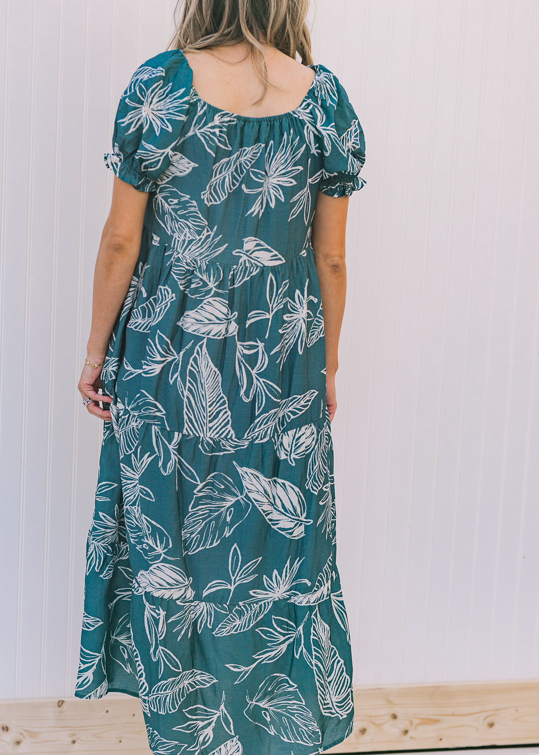 Back view of Model wearing a turquoise midi dress with a cream fern pattern.