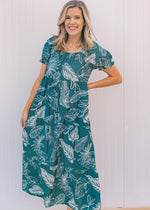 Model wearing a turquoise midi dress with a cream fern pattern and bubble short sleeves. 