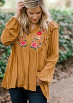 Blonde model wearing mustard blouse with floral embroidery. 