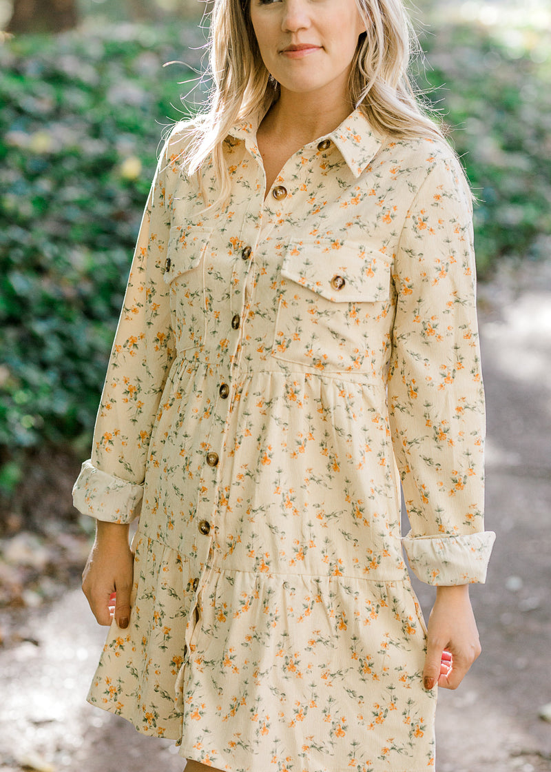 Blonde model wearing cream, button up, corduroy dress with orange floral pattern.