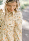 Close up of Blonde model wearing cream corduroy dress with orange floral pattern.