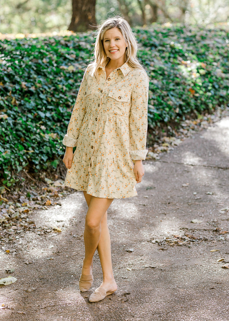 Blonde model wearing cream corduroy dress with orange floral pattern and slip on shoes.