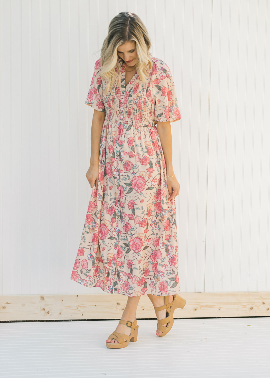 Model wearing a peach, floral, midi dress with a smocked bodice. 
