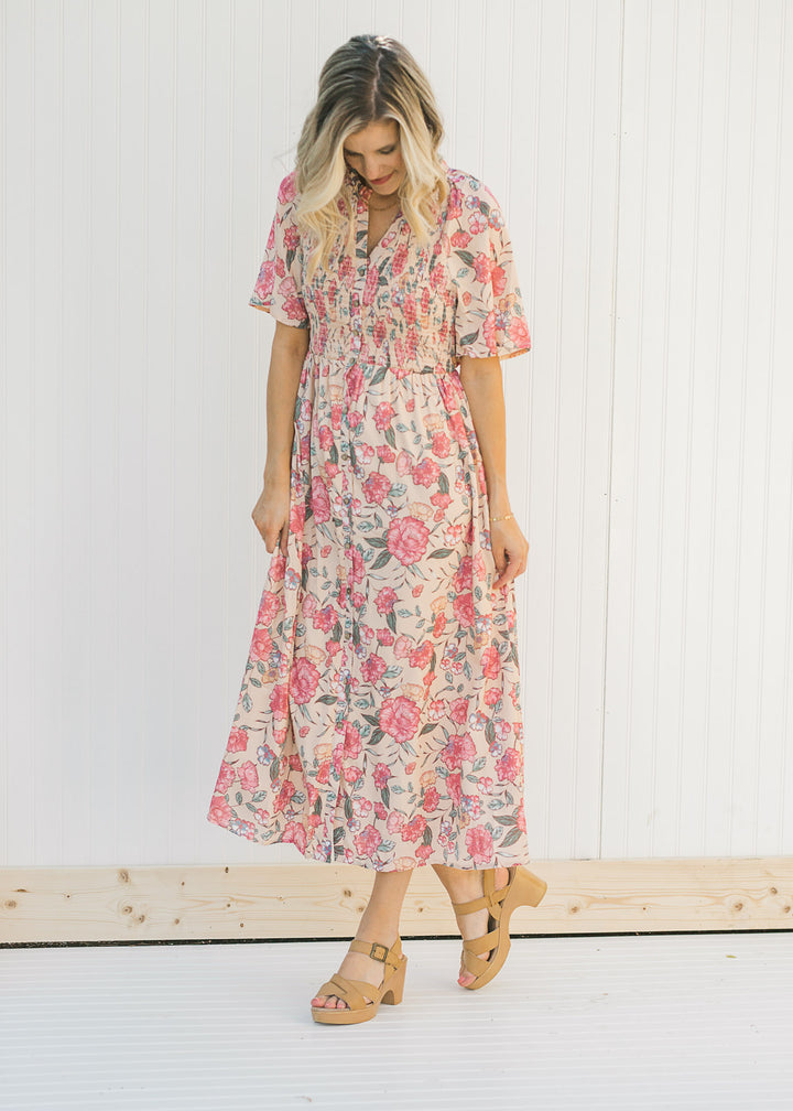 Model wearing a peach, floral, midi dress with a smocked bodice. 