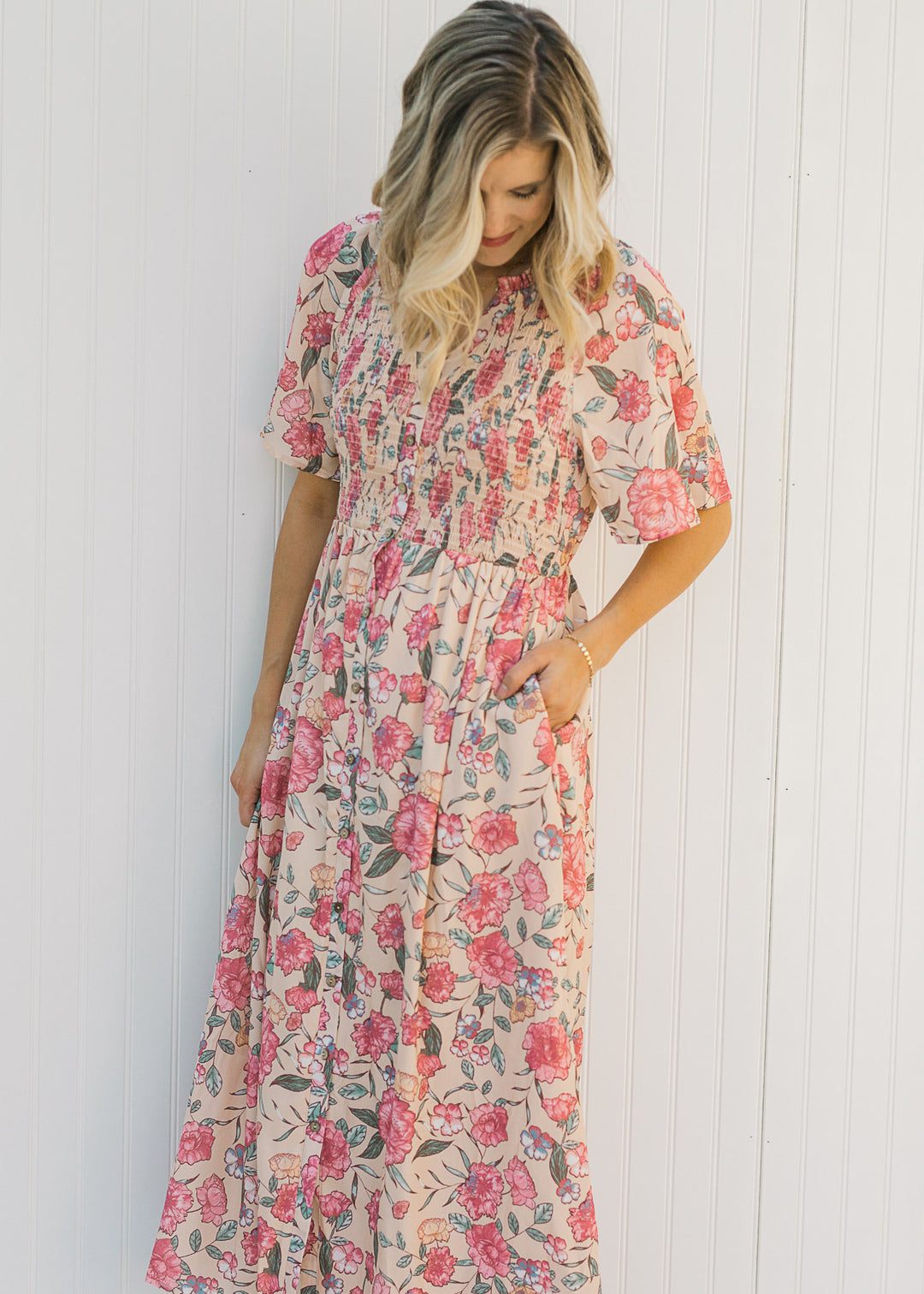 Model wearing a peach, floral, midi dress with a smocked bodice and short sleeves. 