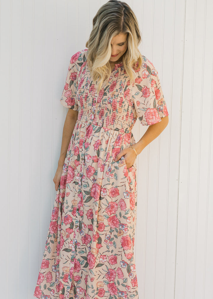 Model wearing a peach, floral, midi dress with a smocked bodice and short sleeves. 