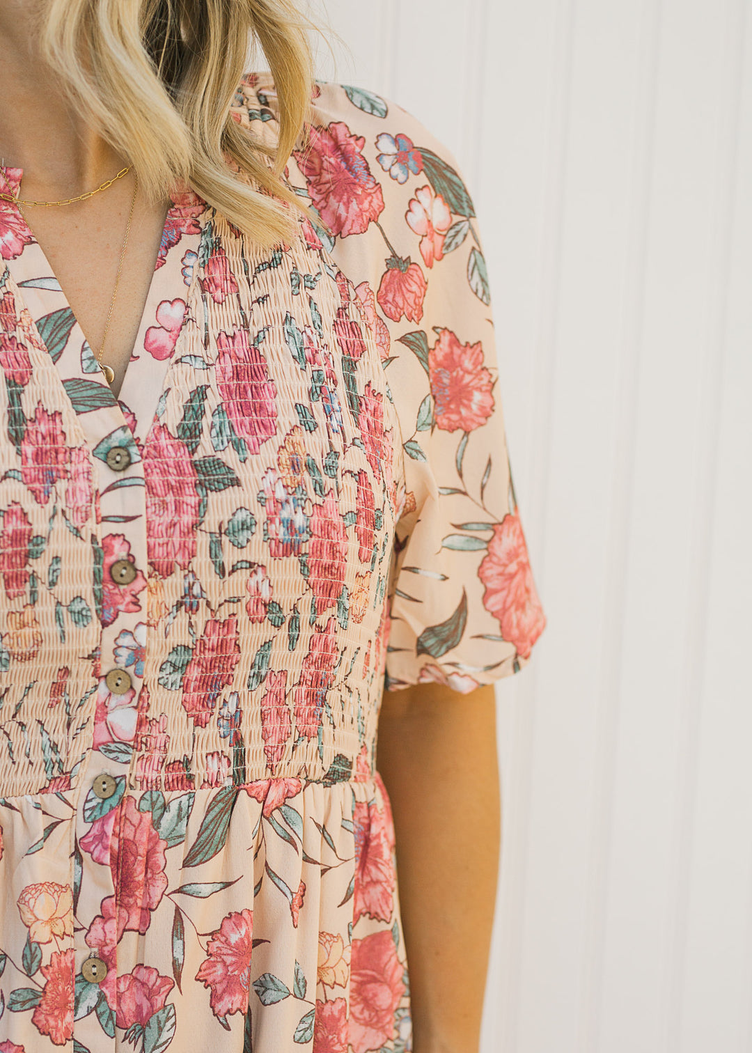 Close up view of smocked bodice and button closure on a peach floral dress. 