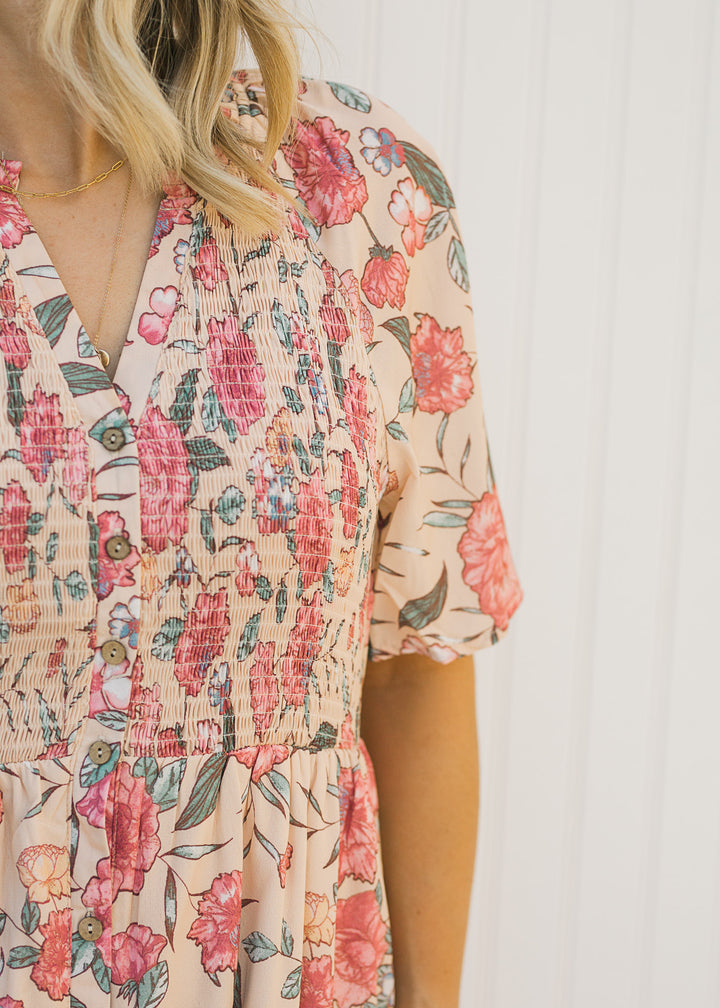 Close up view of smocked bodice and button closure on a peach floral dress. 