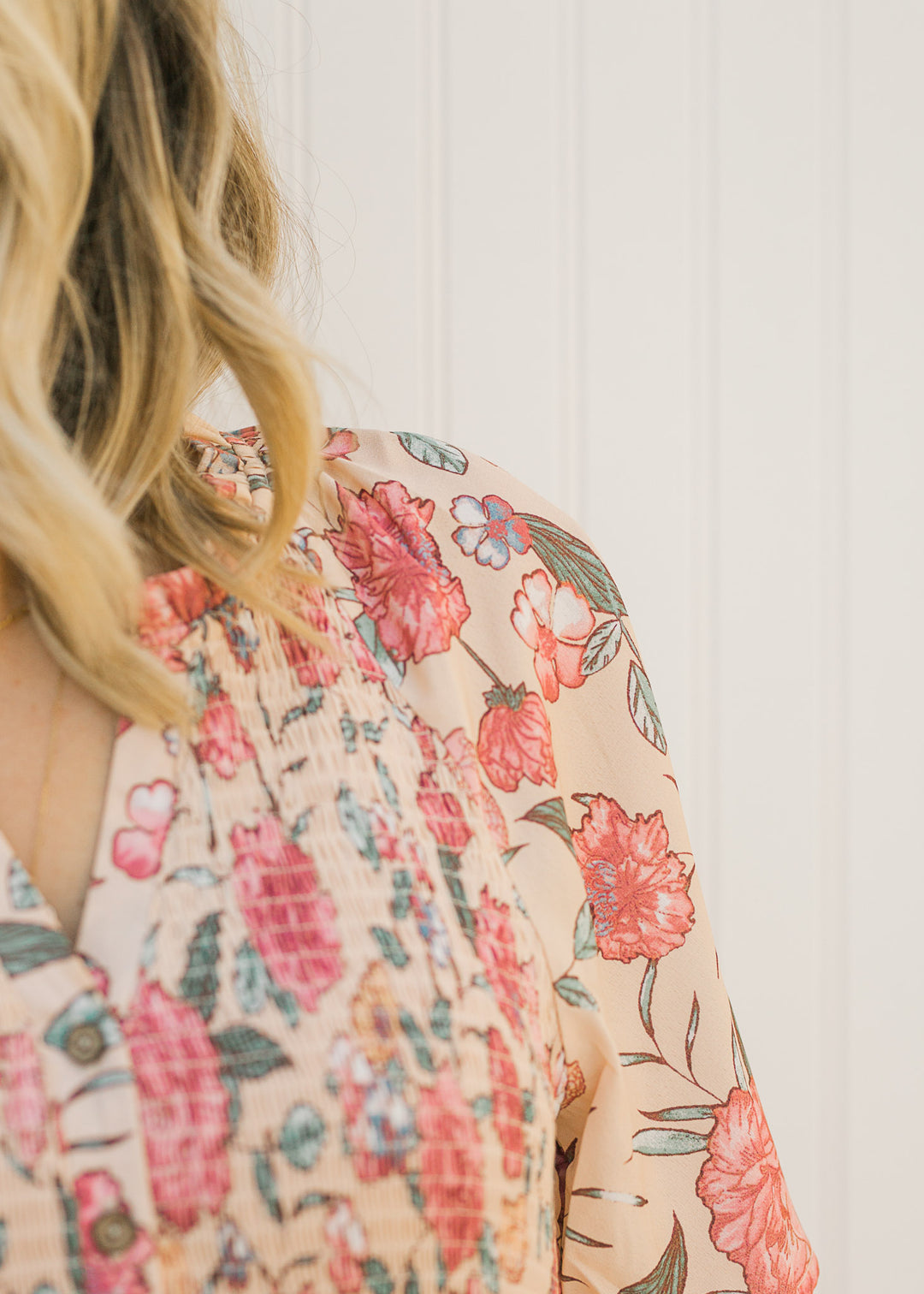 Detail view of Model wearing a peach, floral, midi dress with a smocked bodice.