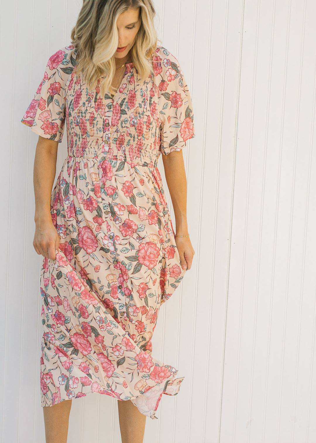 Model twirling a peach, floral, midi dress with a smocked bodice.