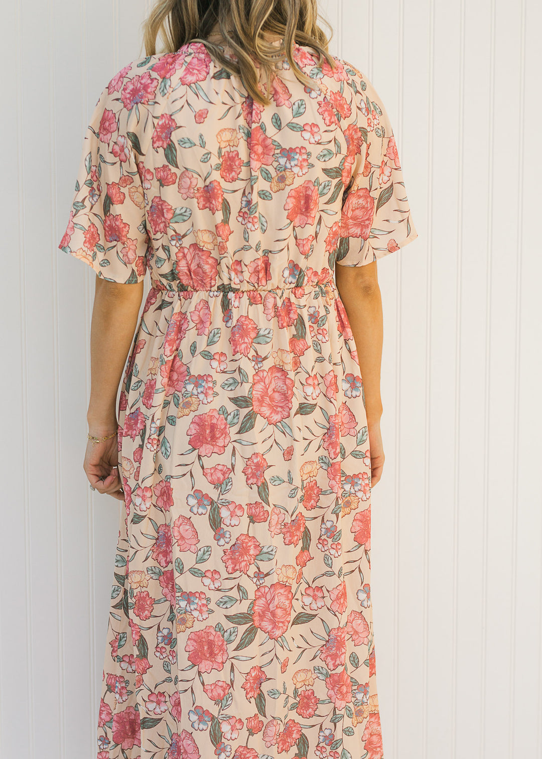 Back view of Model wearing a peach, floral, midi dress with a smocked bodice.