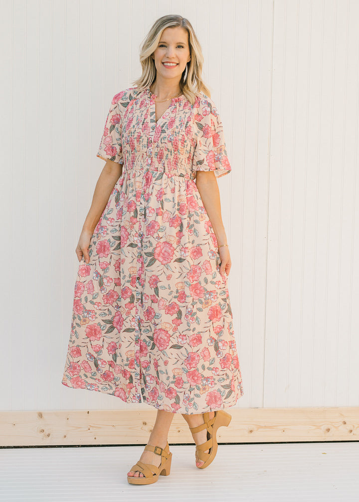 Model wearing a peach, floral, midi dress with a smocked bodice with heels.
