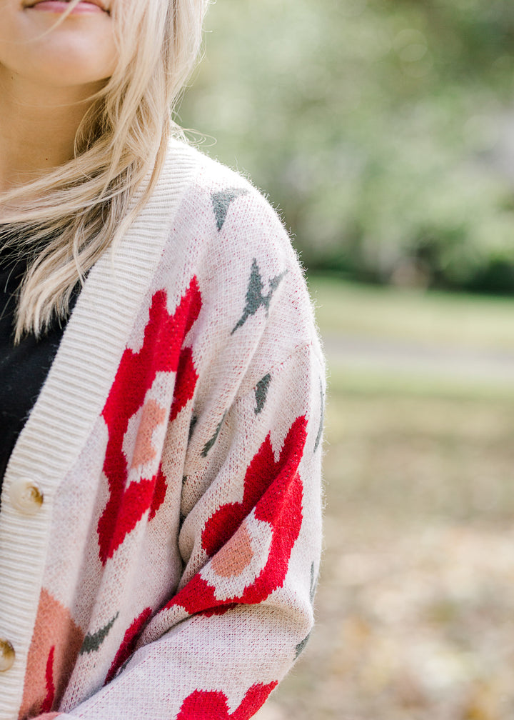 Close up view of Blonde model wearing cream button up cardigan with floral design.