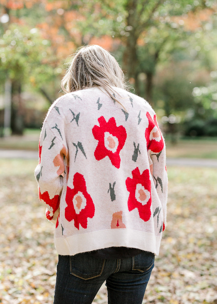 Back view of Blonde model wearing cream button up cardigan with floral design.