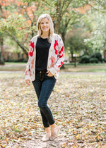 Blonde model wearing black top and jeans with a cream floral design cardigan. 