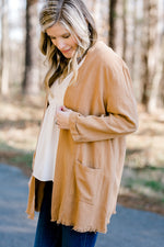 Blonde model wearing in cream blouse with camel colored lightweight jacket.