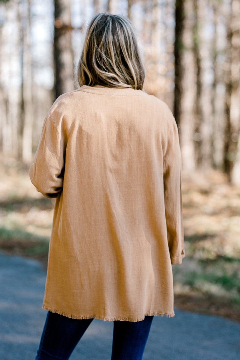 Back view of Blonde model wearing in cream blouse with camel colored lightweight jacket.