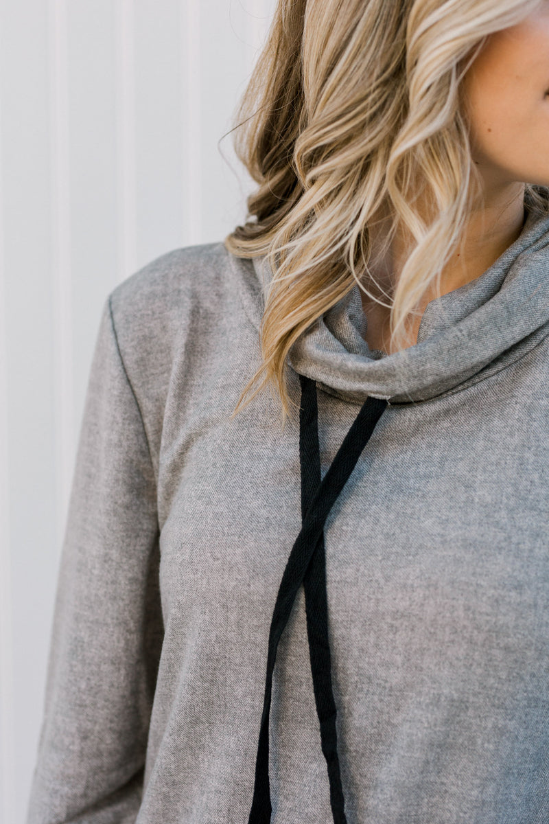 Close up view view of Blonde model wearing a gray top with a tie cowl neck.