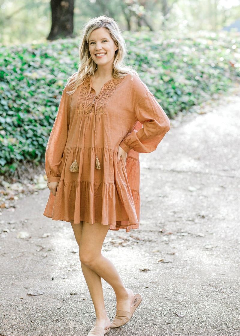 Blonde model wearing ginger colored, above the knee dress with slip on shoes.