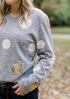 Close up of Blonde model wearing gray sweater with white and gold dots.