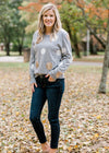 Blonde model wearing gray sweater with white and gold dots and jeans.