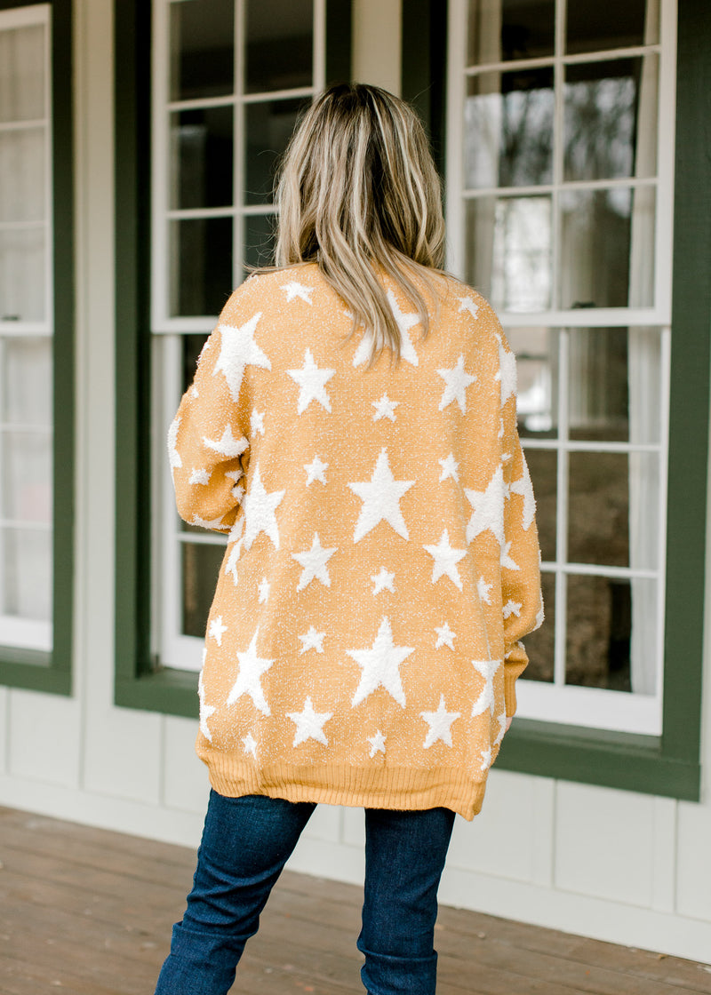 Back view of Blonde model wearing a gold cardigan with cream star pattern. 