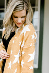 Close up view of Blonde model wearing a gold cardigan with cream star pattern. 