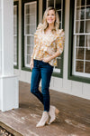 Blonde model wearing golden floral babydoll top with ruffles with jeans and booties.