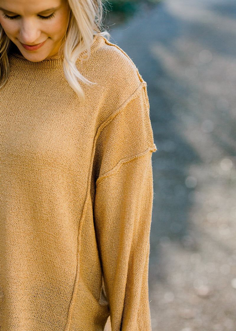 Close up view of exposed hem on honey gold sweater. 
