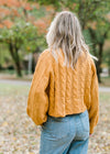 Back view of Blond model wearing gold cropped cable knit sweater.