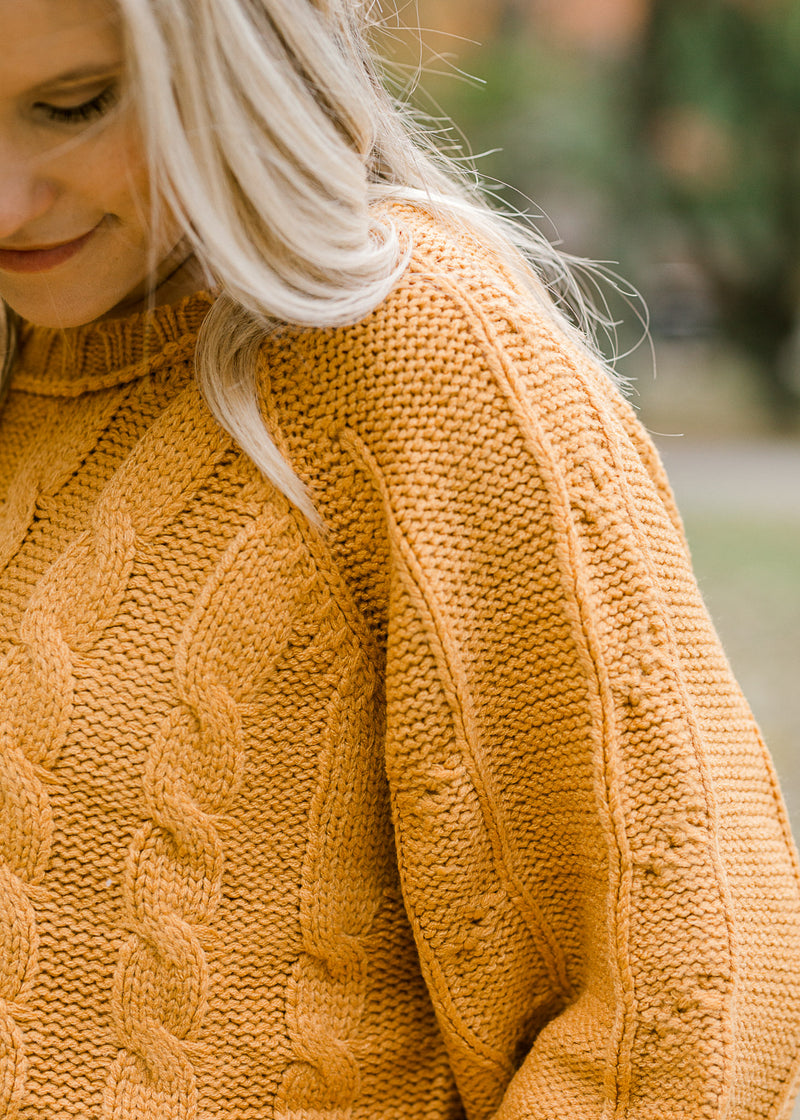 Shoulder detail of Blond model wearing gold cropped cable knit sweater.