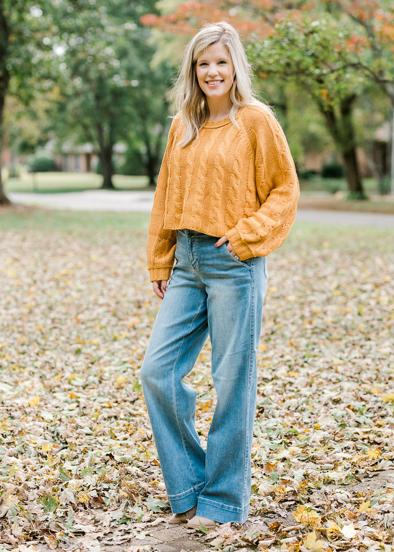 Blond model wearing gold cropped cable knit sweater and jeans.