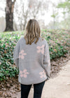 Back view of Blonde model wearing grey sweater with pink flowers.