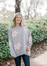 Blonde model wearing grey sweater with pink flowers and jeans.