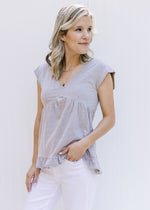 Model wearing a v-neck gray babydoll top with capped sleeves and a tie v-neck in the back.