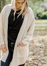 Blonde model wearing cream cardigan with black top and jeans.