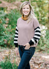 Blonde model wearing a sweater with a taupe bodice and black and white striped sleeves.